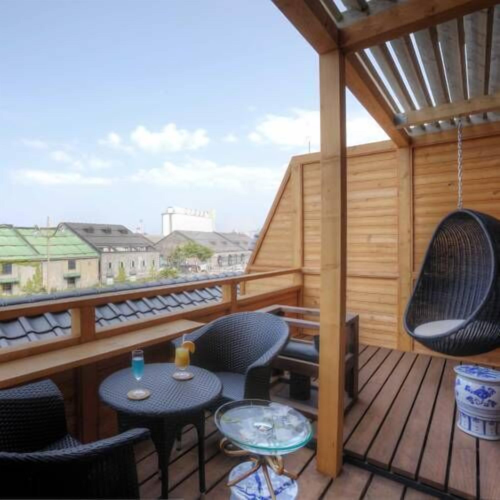 A wooden deck with a table and chairs, a hanging chair, and a view of buildings.