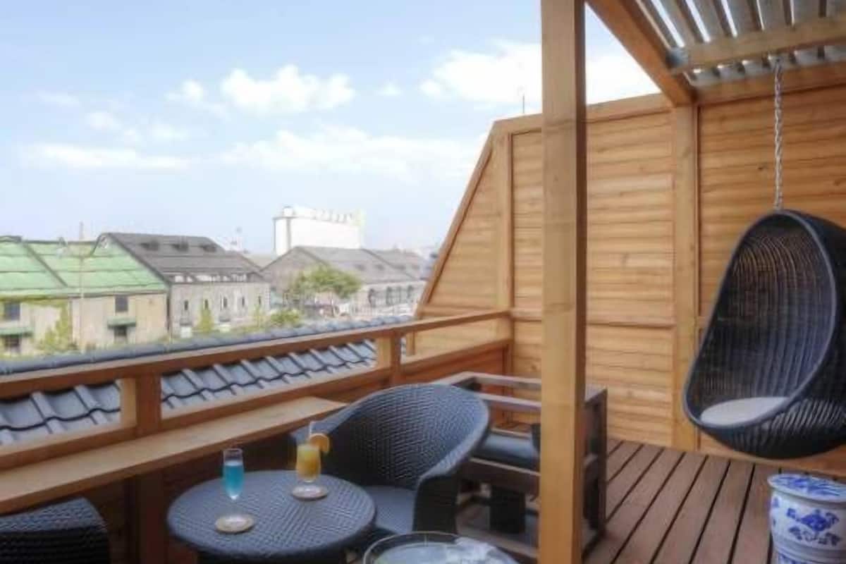 A wooden deck with a table and chairs, a hanging chair, and a view of buildings.