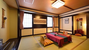 Ett traditionellt japanskt rum med tatamimattor på golvet, en säng med ett rött överkast, ett skrivbord i trä och en skjutdörr.