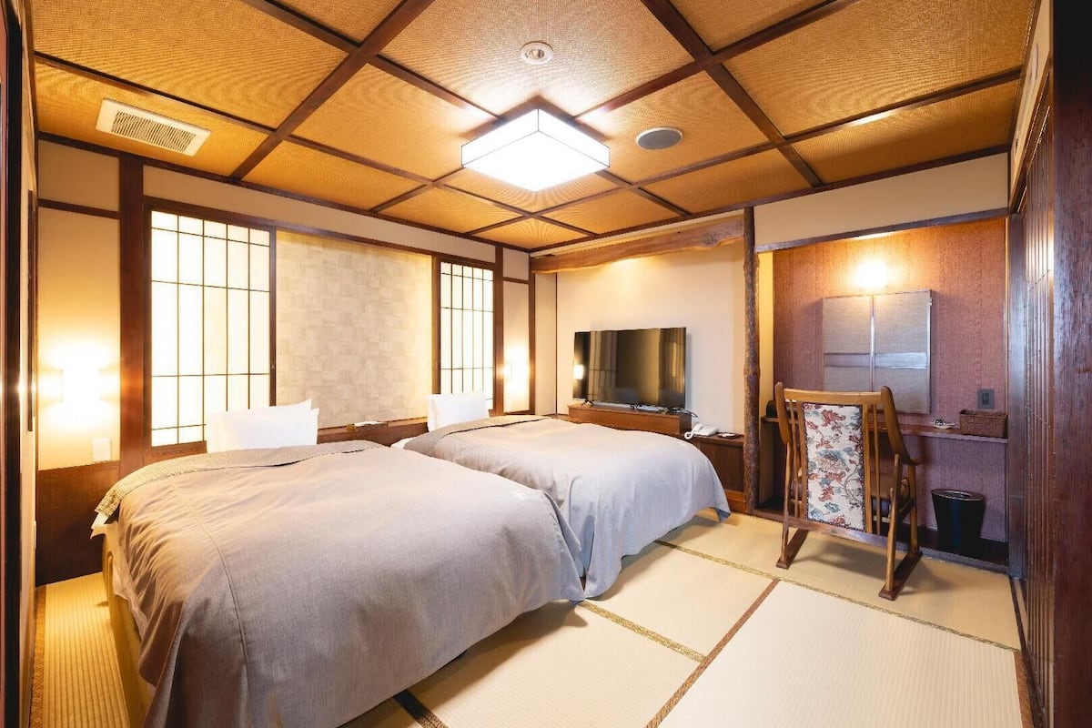 A traditional Japanese-style room with tatami flooring, two beds, a television, and a wooden cabinet.
