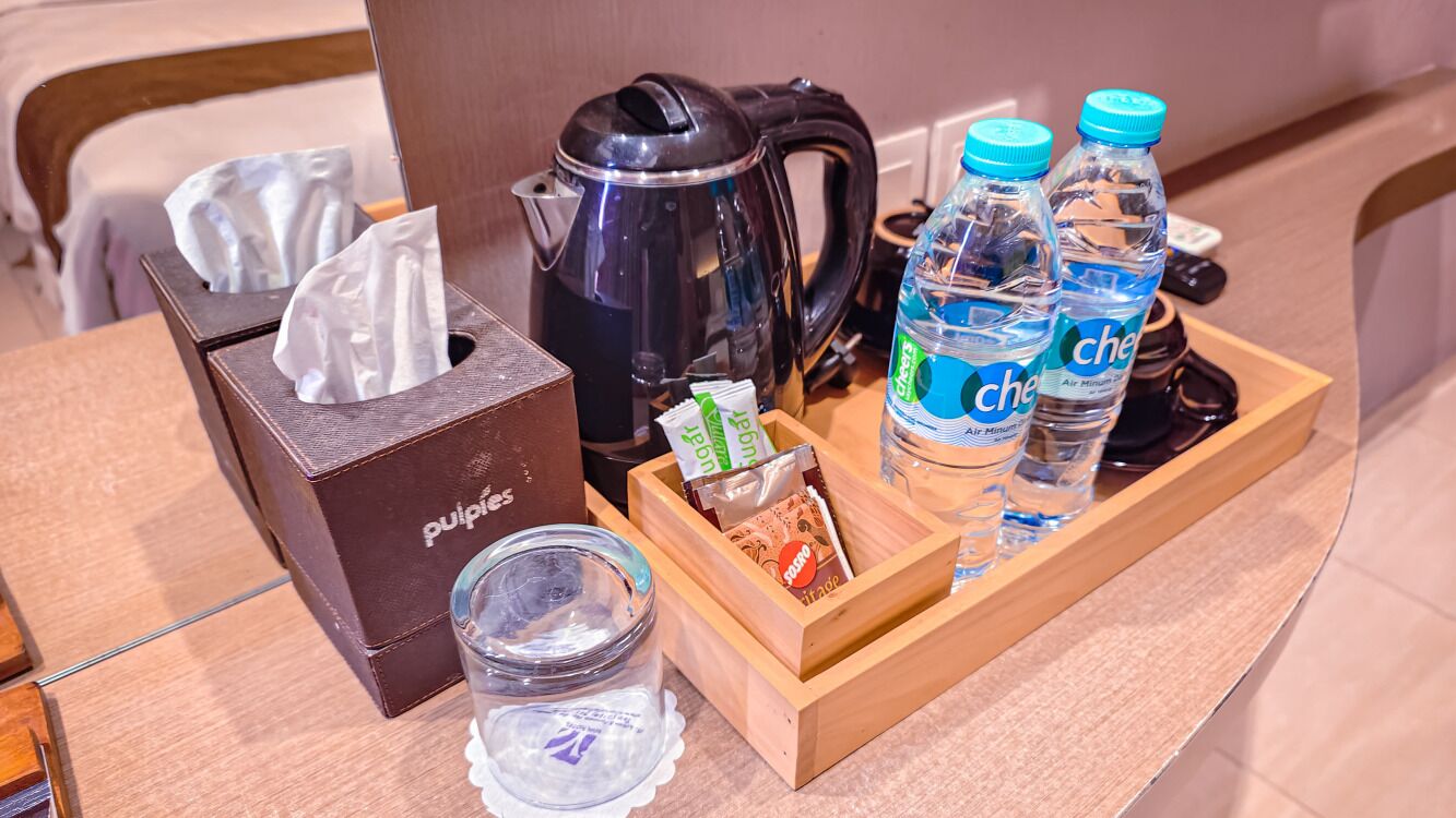 Ontbijfwagen in een hotelkamer, met zakdoekjes, een koffiezetapparaat, waterflesjes en een glas.