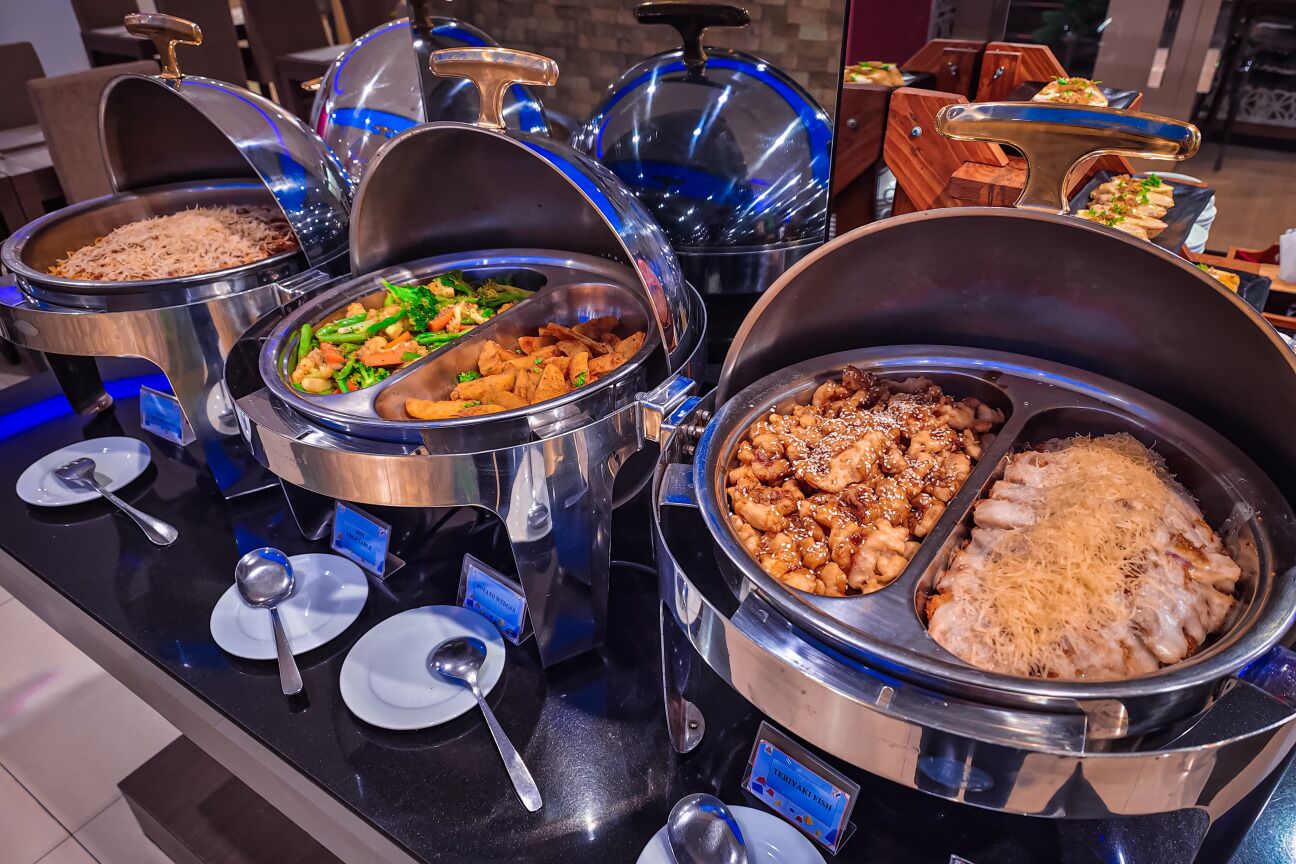 A buffet with various dishes in large metal containers, including rice, vegetables, and meat.