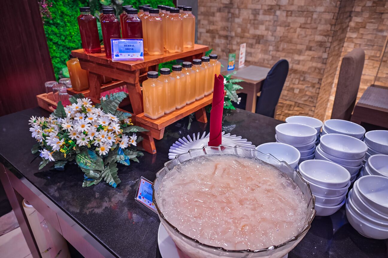 Una mesa de buffet con diversas bebidas, incluyendo un gran bol de agua helada, una decoración floral y una presentación de bebidas embotelladas.