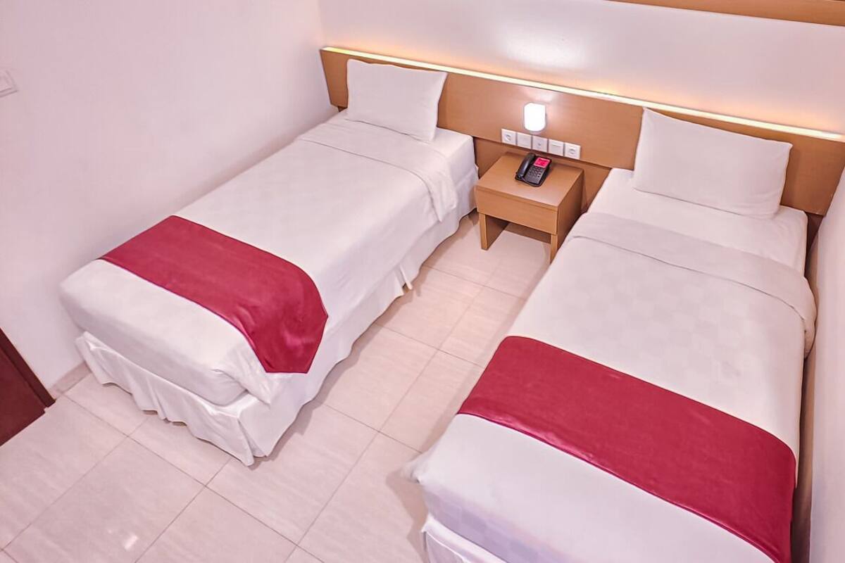 Een hotelkamer met twee enkele bedden, een nachtkastje met telefoon en een bedlampje.