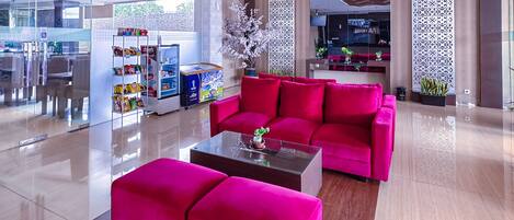 A modern lobby with a bright, spacious layout, featuring a red sofa and ottoman, a glass coffee table, and a vending machine.