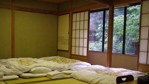 A traditional Japanese room with tatami flooring, a low wooden table, and a bed with a floral bedspread.