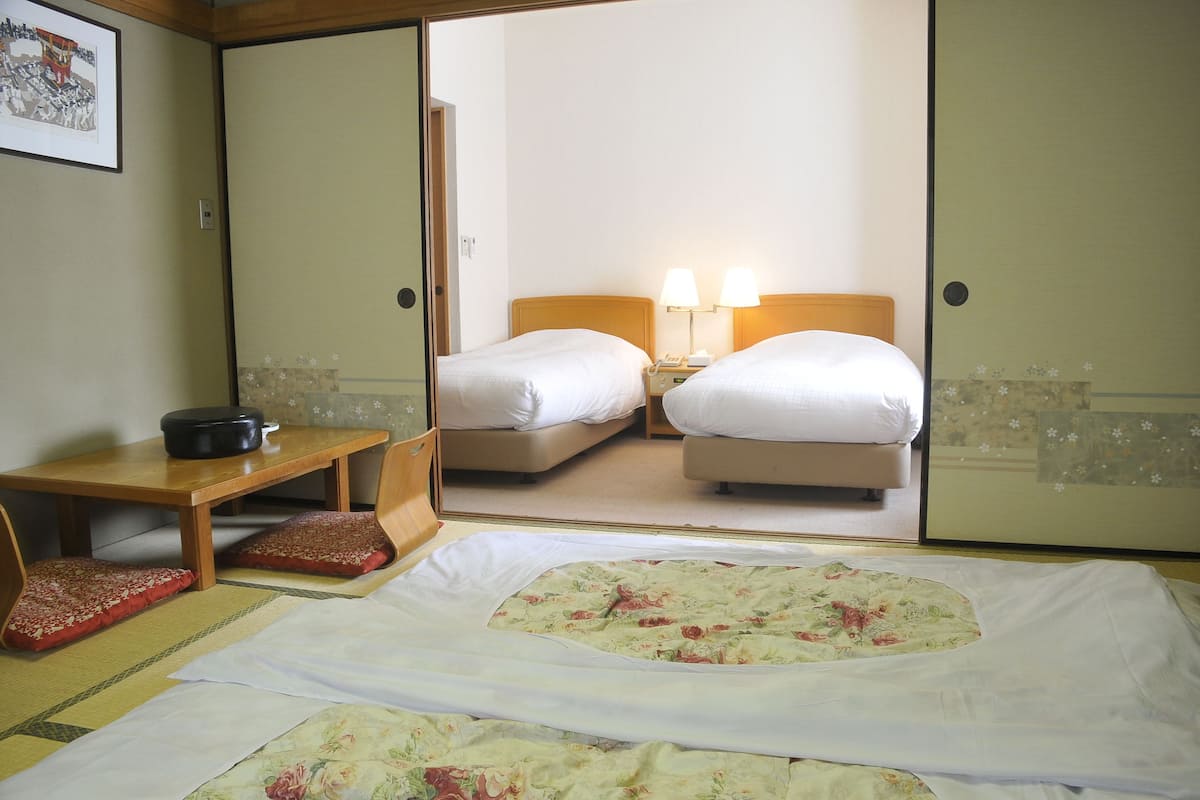 Habitació d'hotel amb dos llits, una taula de fusta i un mirall que reflecteix l'habitació.