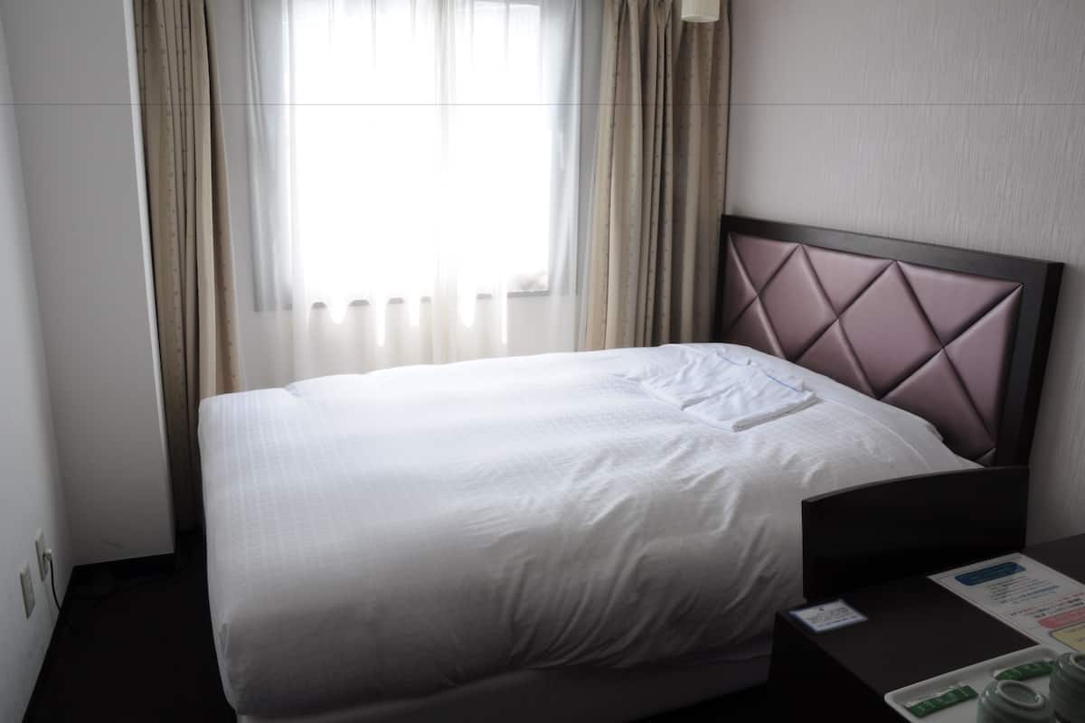 Una habitació d'hotel amb un llit ben fet, una taula de nit amb un menú i una finestra amb cortines.