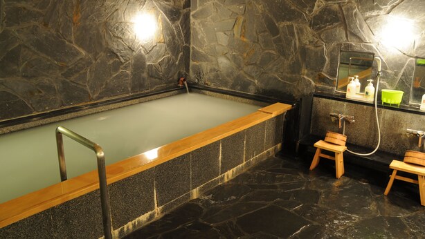 A stone-walled bathroom with a bathtub, wooden stools, and a mirror.