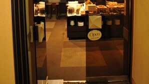A restaurant entrance with a glass door, a clock on the wall, and a sign indicating the restaurant is open.