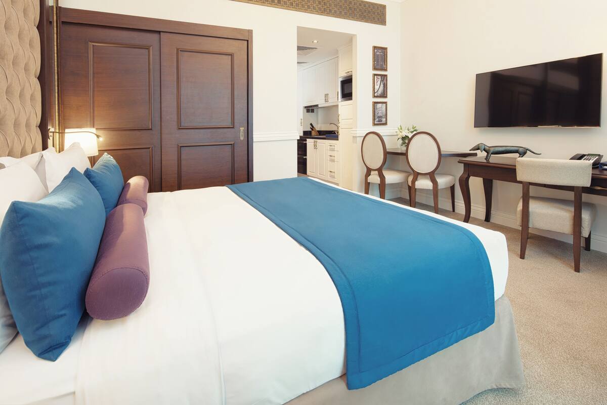 A hotel room with a bed, a desk, a chair, a television, and a kitchen area.