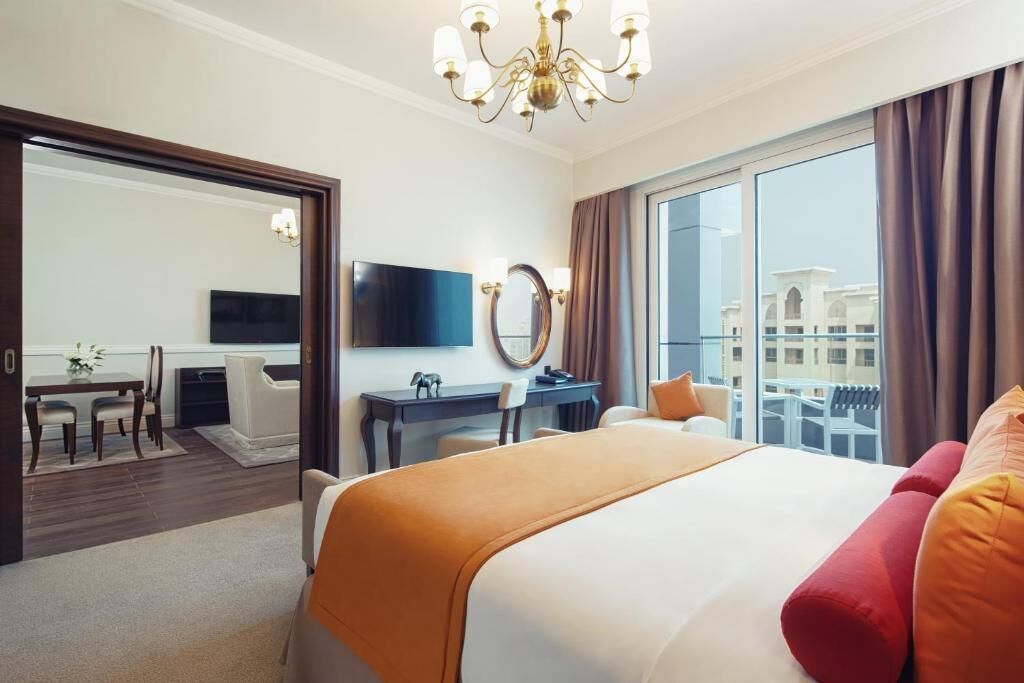 A hotel room with a large bed, a desk, a chair, a TV, and a view of buildings through the window.