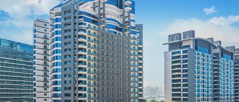 A modern high-rise hotel with multiple balconies, a central courtyard, and a view of the city skyline.
