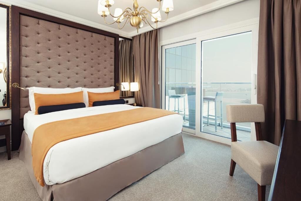 Habitación de hotel con una cama grande, un candelabro, un balcón con vistas y una silla.