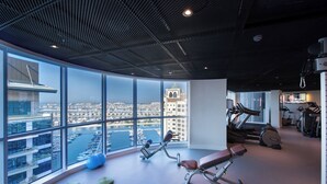 Un gimnasio moderno con amplias ventanas, equipamiento de ejercicio y vistas a un paisaje urbano.