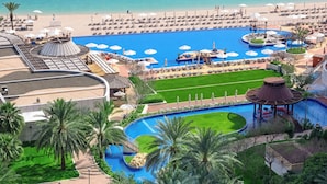 Un resort con una piscina grande, zona de playa y palmeras.