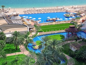 Un resort con una piscina grande, zona de playa y palmeras.