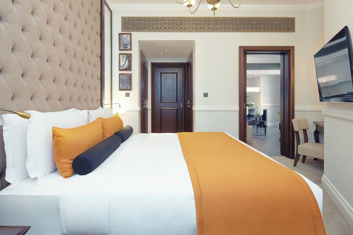 A hotel room with a large bed, a tufted headboard, a television, and a door leading to a bathroom.
