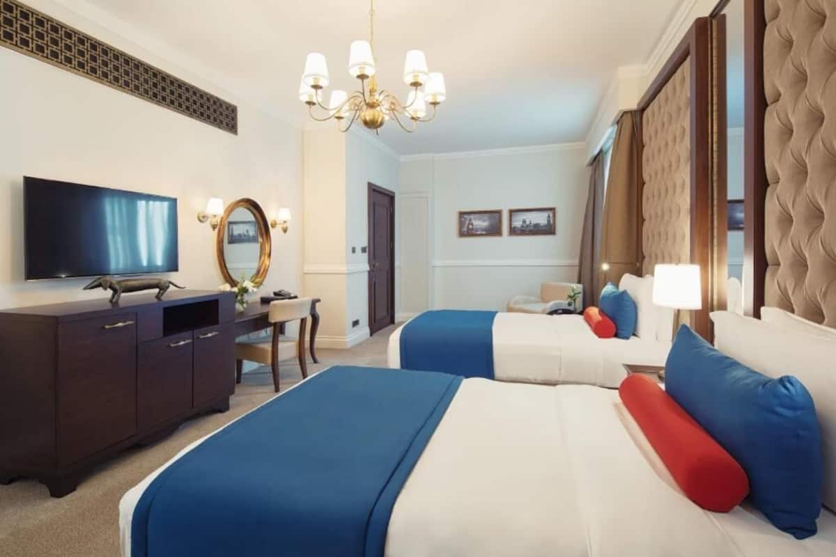 A hotel room with two beds, a TV, a desk, and a large mirror.