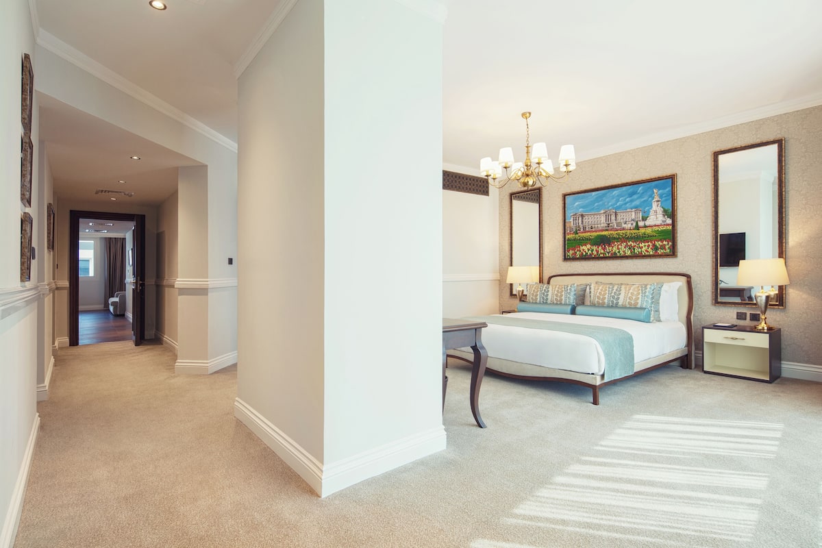 A hotel room with a large bed, a chandelier, a painting on the wall, and a mirror.