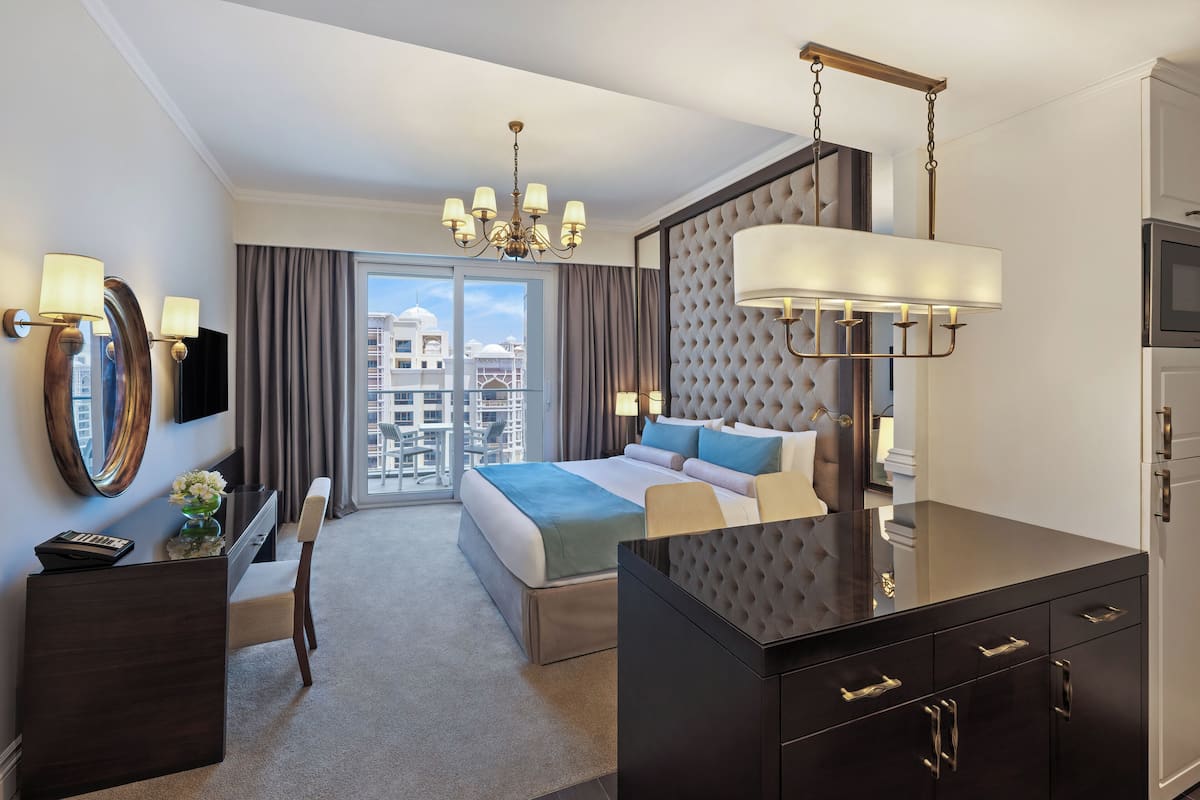 A hotel room with a large bed, a desk with a chair, a TV, a minibar, and a view of the city.