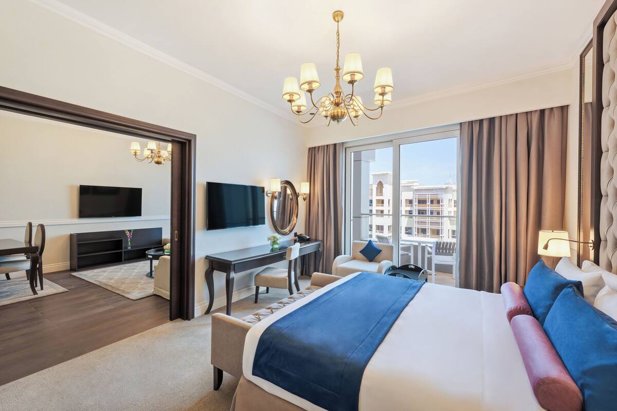 A modern hotel room with a large bed, a desk, a television, and a balcony with a city view.