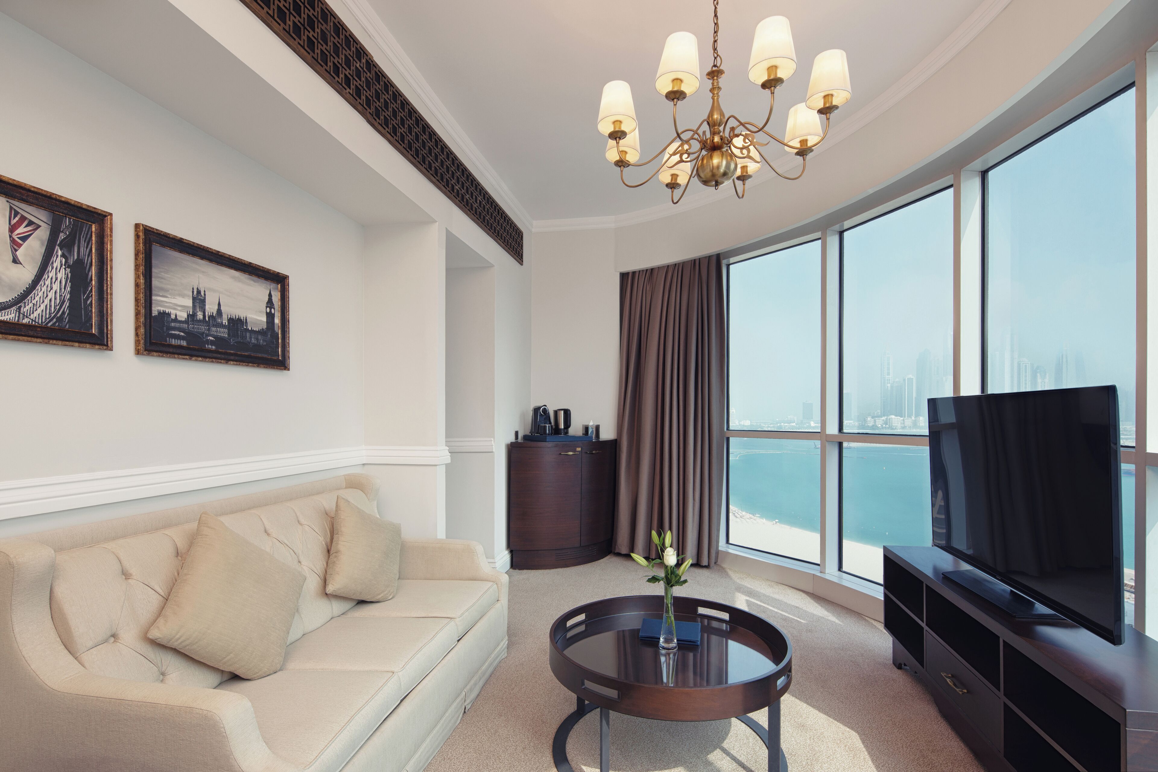 A modern living room with a sofa, a coffee table, a TV, and large windows offering a city view.