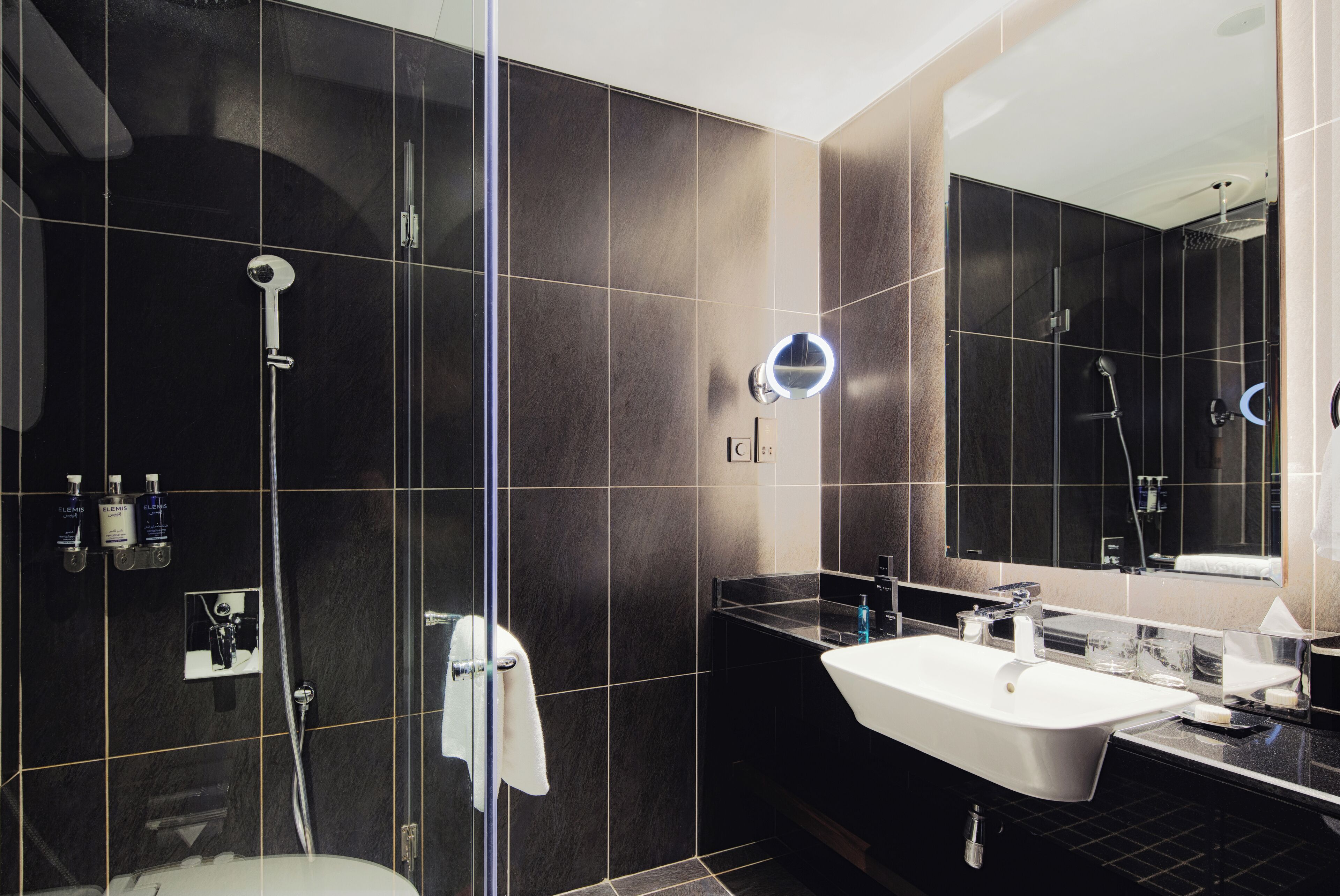 Ein modernes Badezimmer mit einer gläsernen Dusche, einem weißen Waschbecken und einem großen Spiegel.