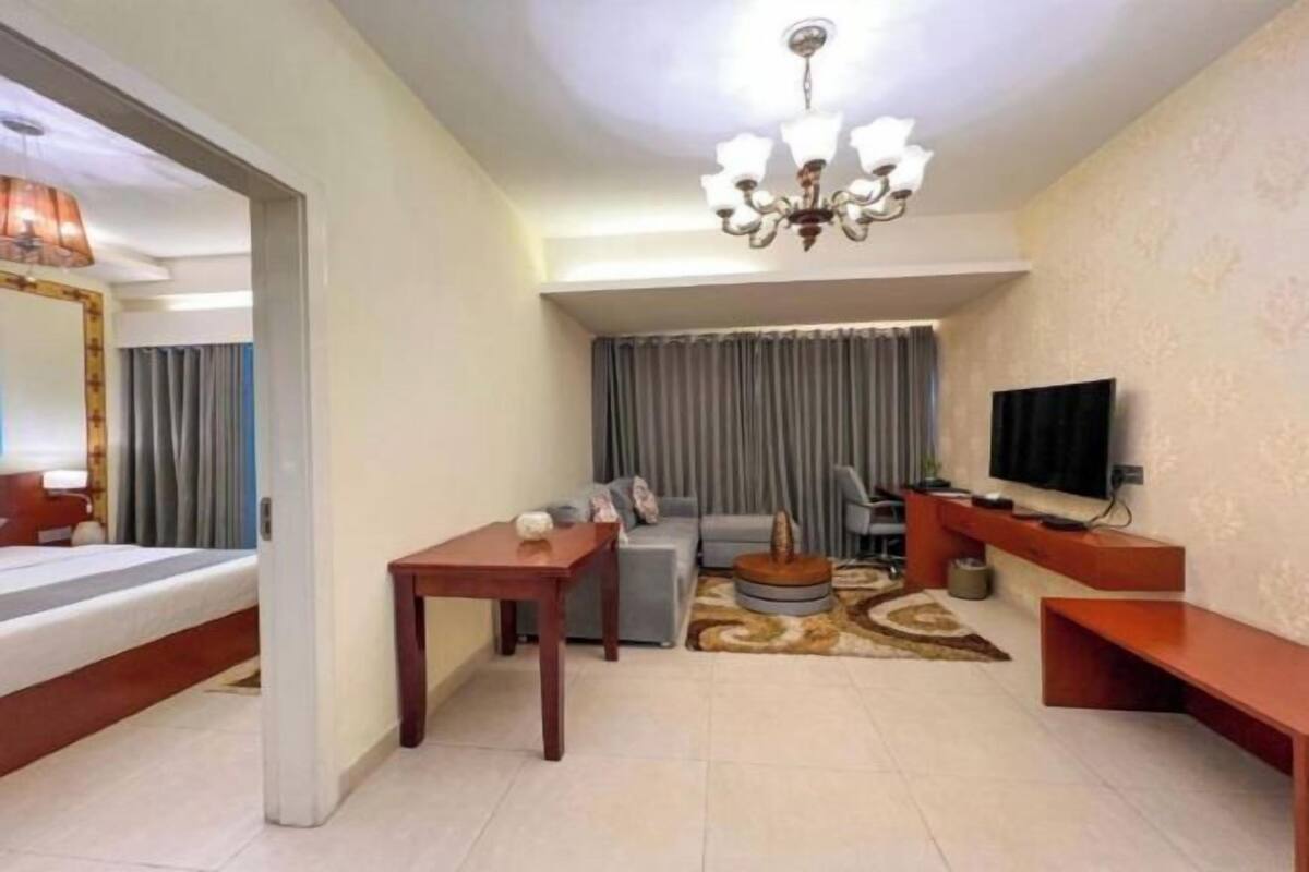 A hotel room with a bed, a sofa, a TV, a table, and a chandelier.