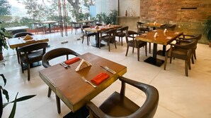 A restaurant with multiple tables and chairs, a stone wall, and a view of trees through large windows.