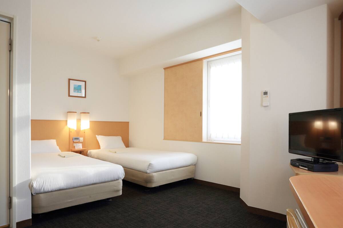 Quarto de hotel com duas camas, uma televisão e uma janela.