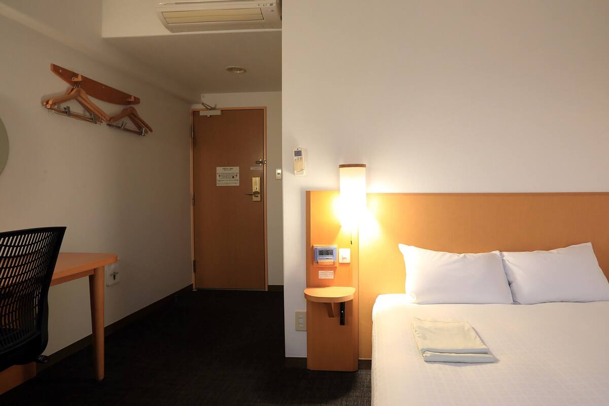 Quarto de hotel com cama, mesa de cabeceira, abajur e uma cadeira.