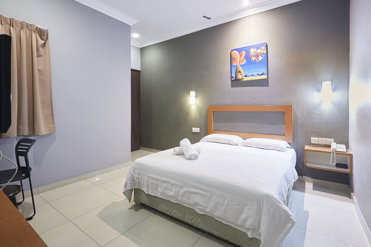 Une chambre d’hôtel avec un lit, une chaise, une table de chevet avec un téléphone et un tableau au mur.