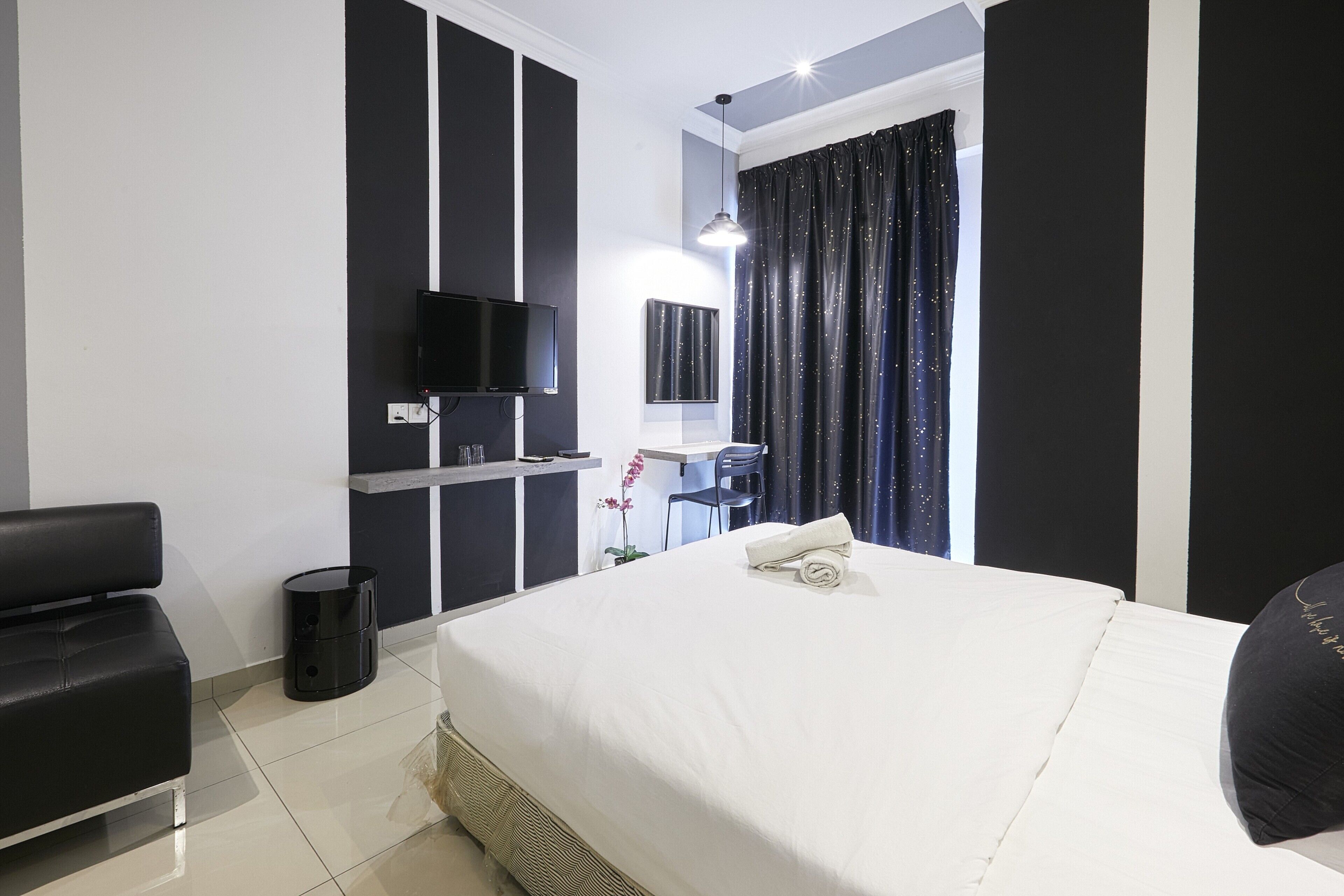 A hotel room with a large bed, a desk with a chair, a television, and a window with curtains.