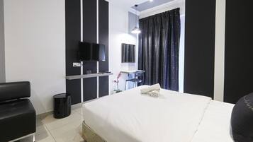 A hotel room with a large bed, a desk with a chair, a television, and a window with curtains.