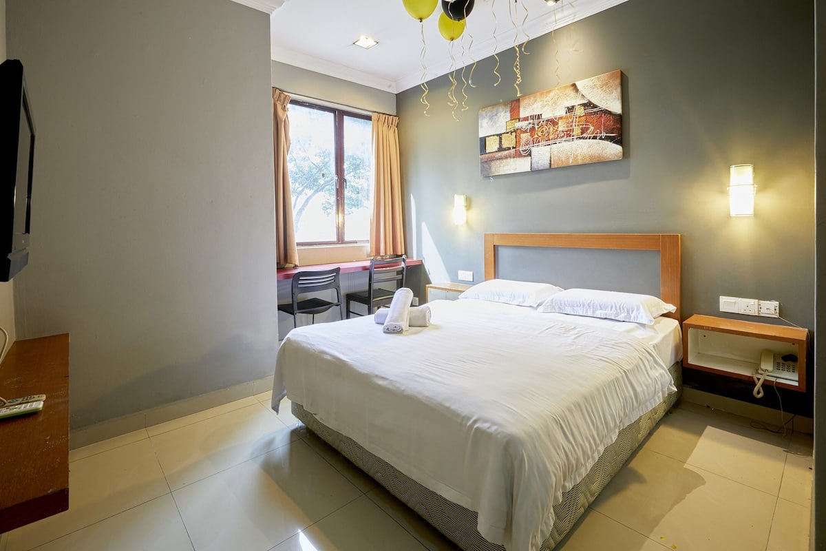 Une chambre d’hôtel avec un grand lit, un bureau avec une chaise, une fenêtre avec des rideaux et une œuvre d’art accrochée au mur.