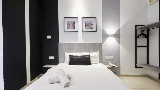 Een hotelkamer met een net opgemaakt bed, een nachtkastje met lamp, een wandplank en twee ingelijste foto's boven het bed.