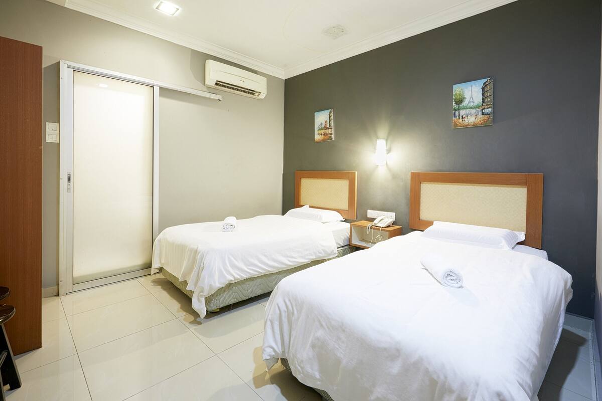 Une chambre d’hôtel avec deux lits, une porte, un appareil de climatisation et une table de chevet avec un téléphone.