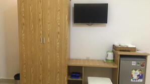 Una habitación con un armario de madera, un escritorio pequeño con una silla, un televisor montado en la pared y un refrigerador con imanes.