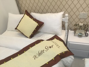 A hotel room with a neatly made bed, a decorative pillow, a bedside telephone, and a wall with a diamond-patterned design. - White Star Hotel (Xuan Huong - Da Lat)