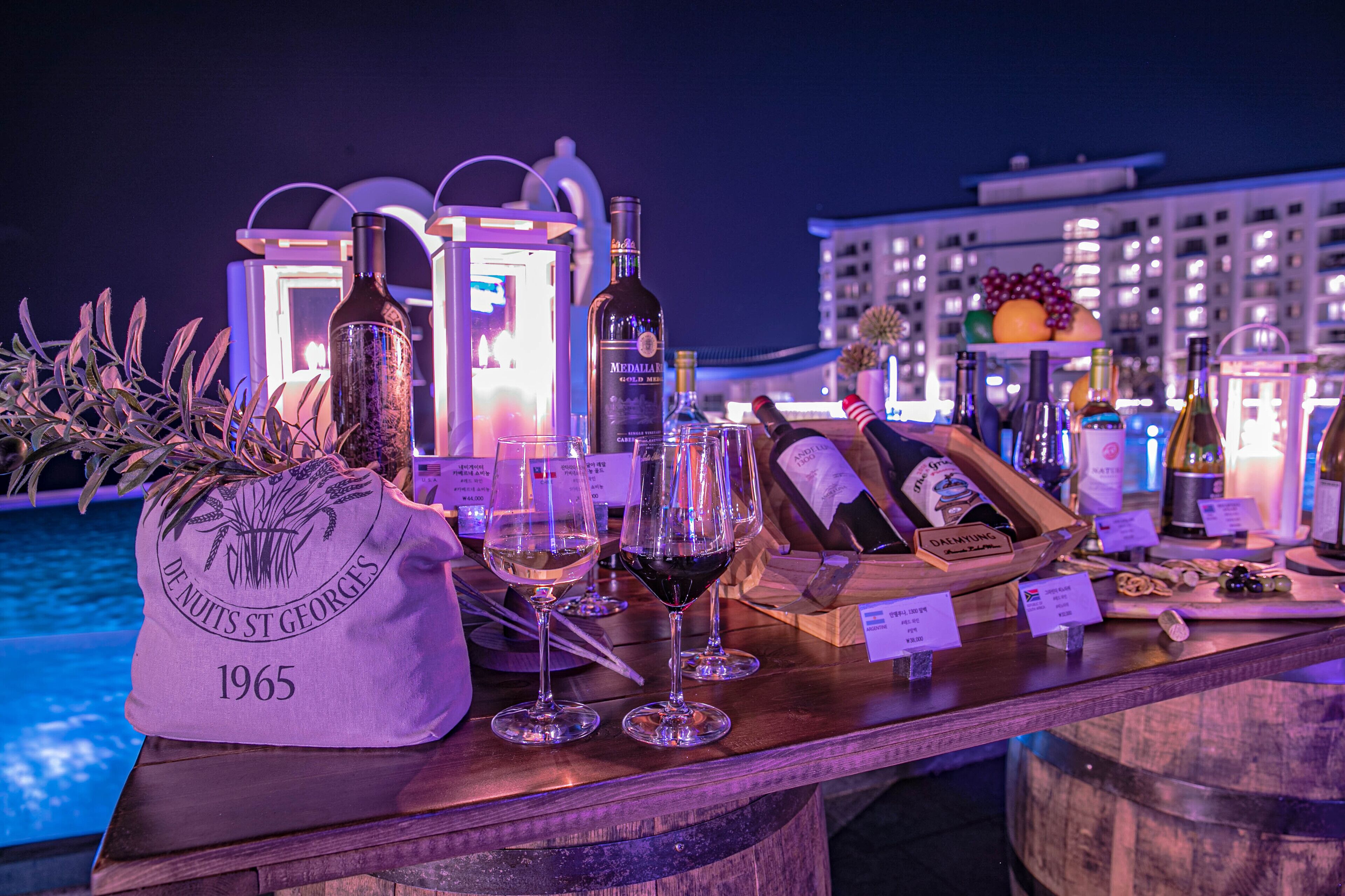 A bar area with wine glasses, bottles, and a bag labeled "Dunottis St. Georges 1965" near a pool.