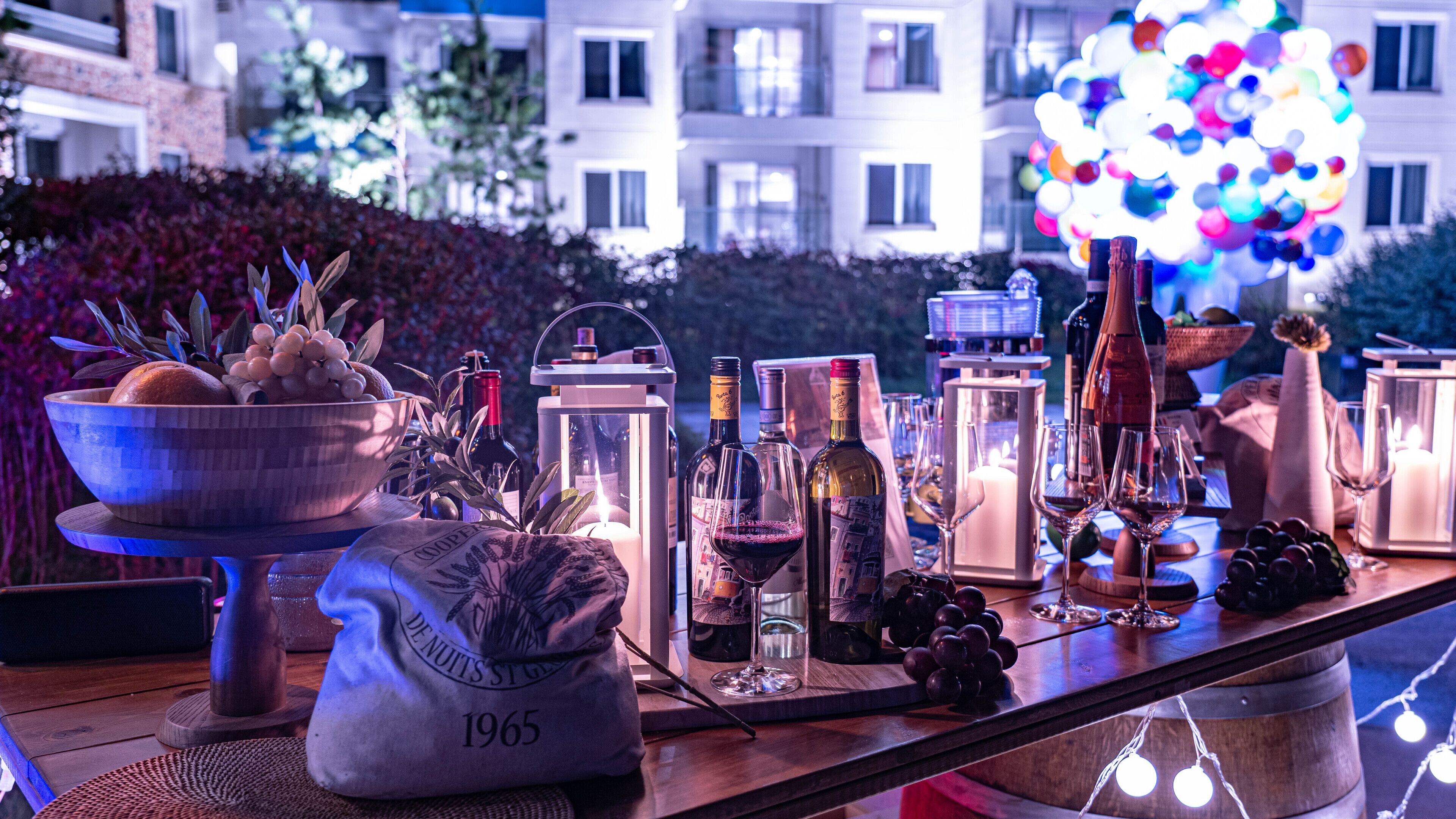 Une table dressée avec des bouteilles de vin, des verres et un saladier rempli de fruits.