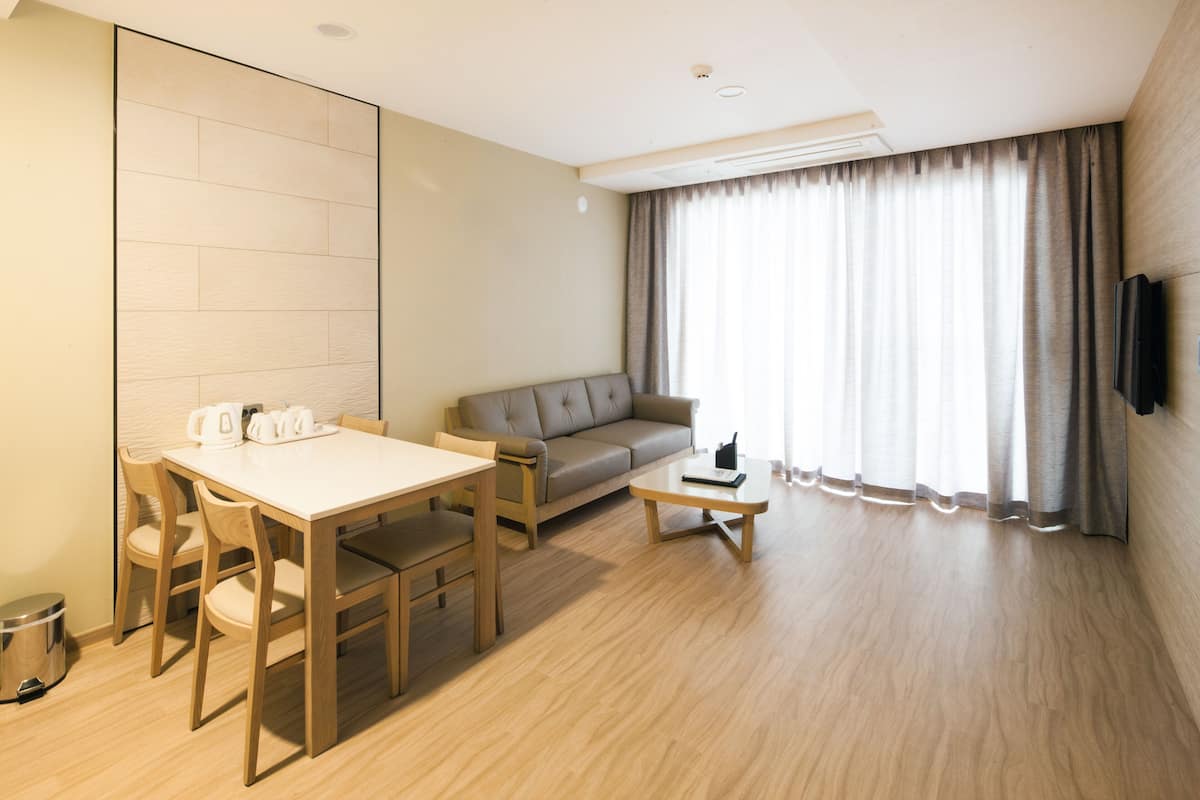 A modern living room with a sofa, a dining table with chairs, a coffee table, and a television mounted on the wall.