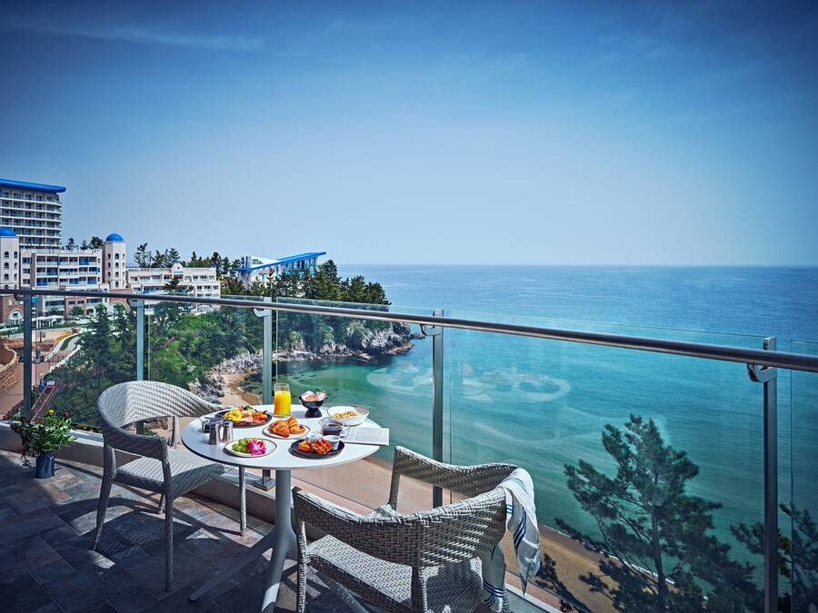 A balcony with a table set for breakfast overlooking a coastal view.