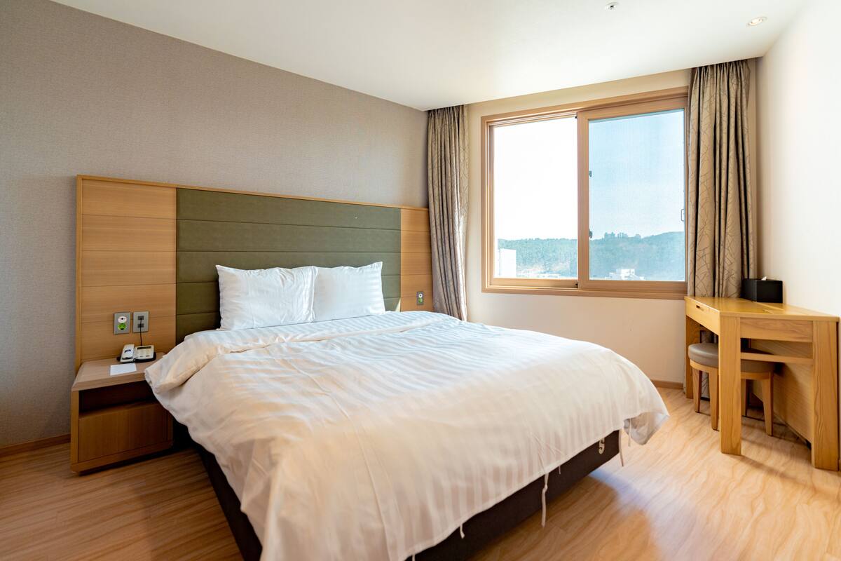 A hotel room with a large bed, a desk, and a window with curtains.