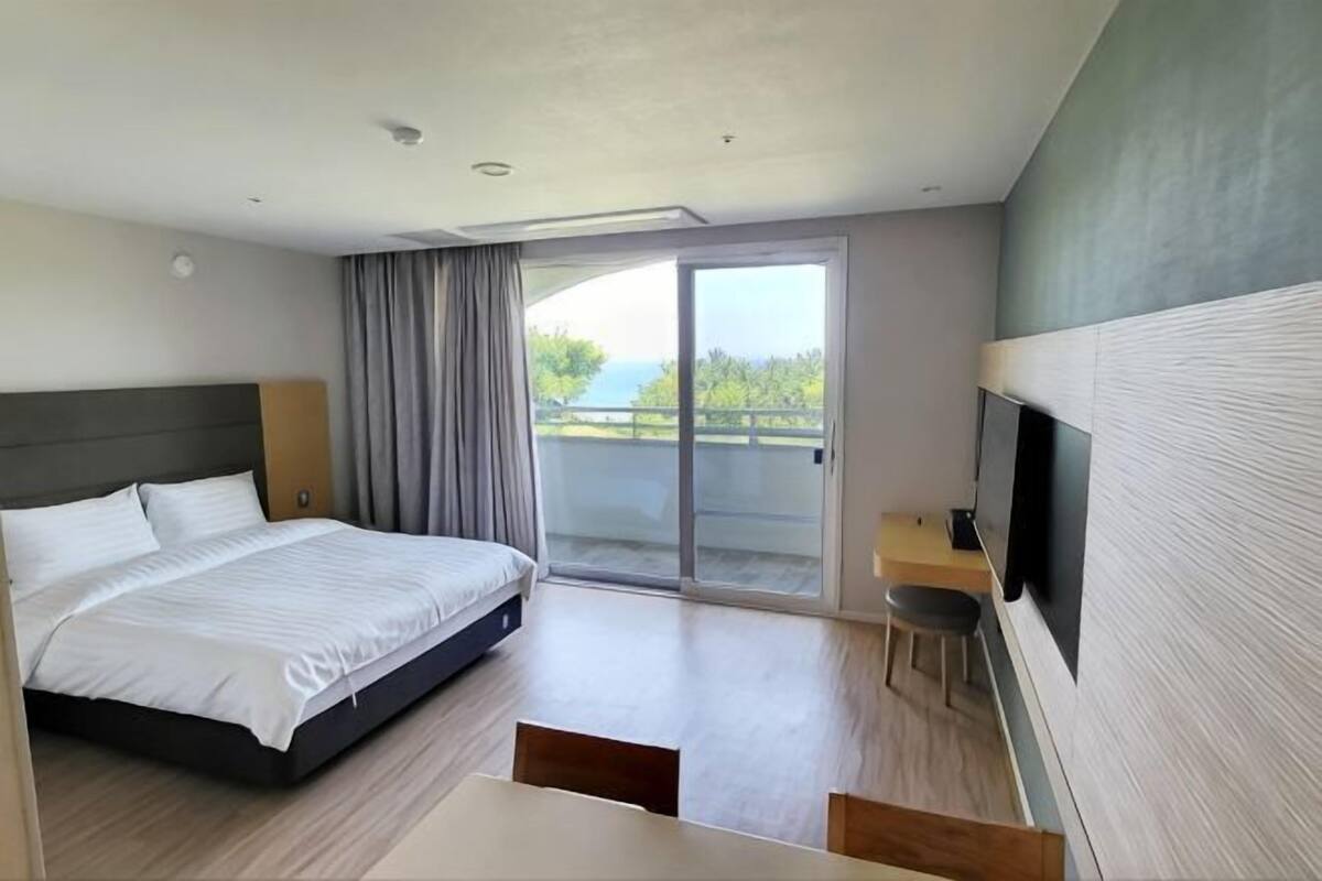 A hotel room with a bed, a desk, a chair, a TV, and a sliding glass door to the outside.