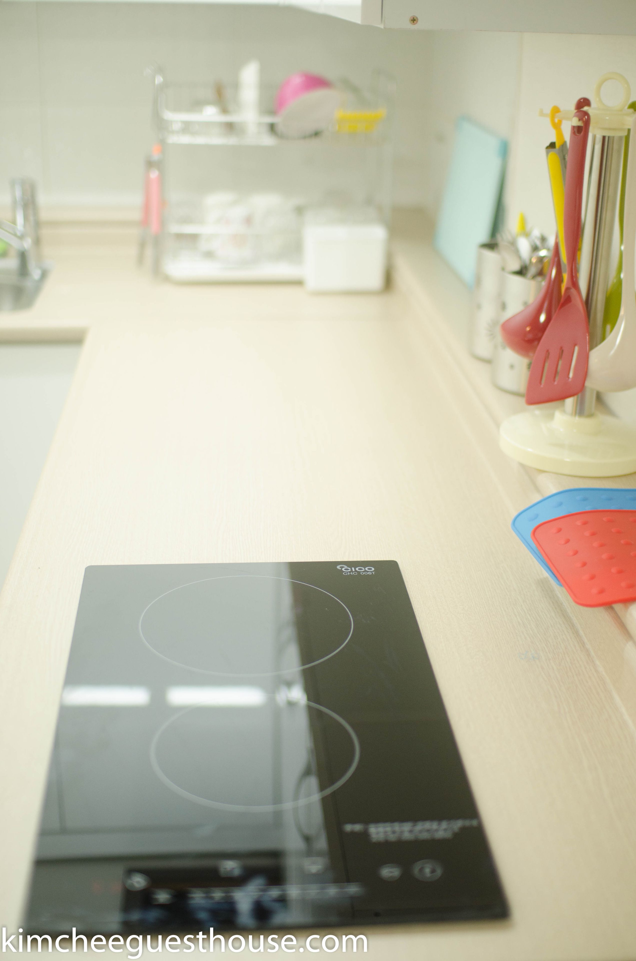 A kitchen with a black induction cooktop, a white countertop, and various kitchen utensils and appliances.