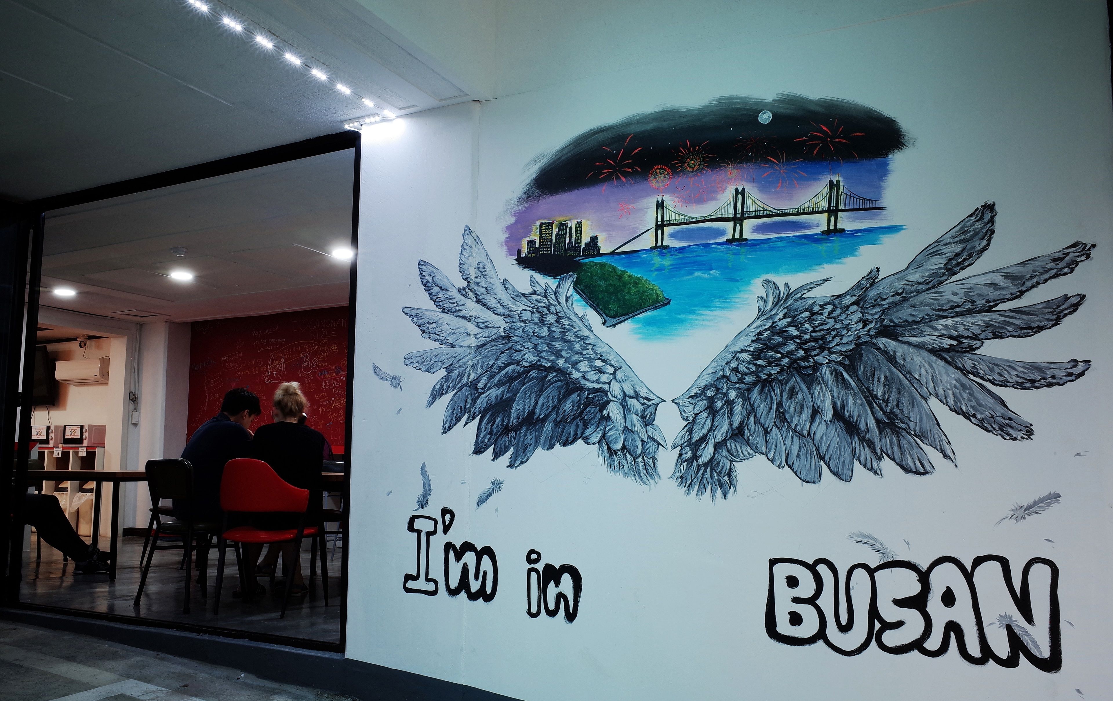 Un mur orné d’une fresque représentant un pont et des feux d’artifice, avec l’inscription : « J’aime BUSAN ».