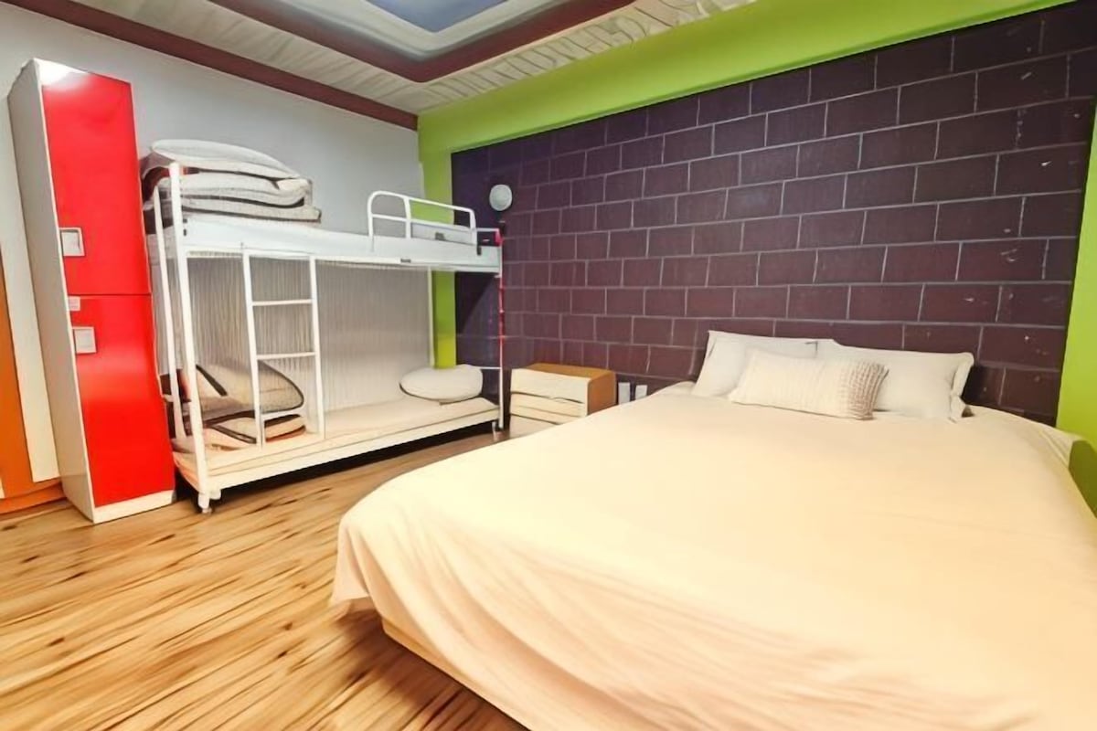 A room with a bunk bed, a single bed, a red wardrobe, and a brick-patterned headboard.