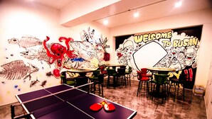 A room with a ping pong table, colorful chairs, and walls decorated with various murals and graffiti. - Kimchee Busan Downtown Guesthouse - Hostel (Busan)